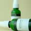 Two green bottles with white labels on a beige background