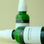 Two green bottles with white labels on a beige background